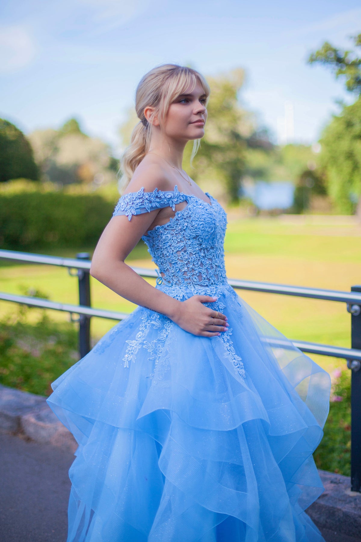 Tämä upea sky blue -sävyinen vanhojentanssimekko hurmaa elegantilla off shoulder -yläosalla, kauniilla pitsiyksityiskohdilla ja näyttävällä röyhelöhelmalla.