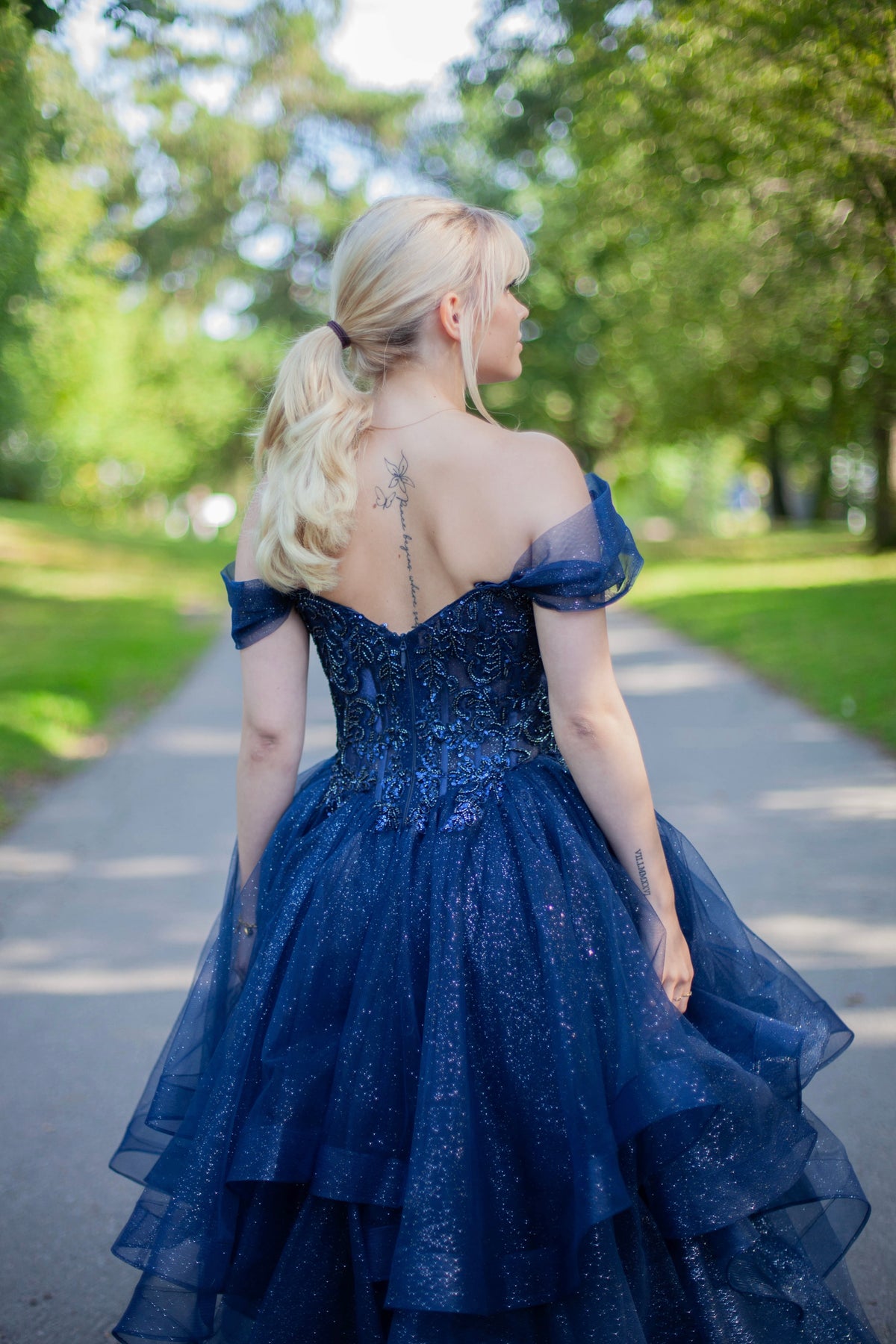 Kimaltava tummansininen vanhojentanssimekko off shoulder -yläosalla ja näyttävällä röyhelöhelmalla.