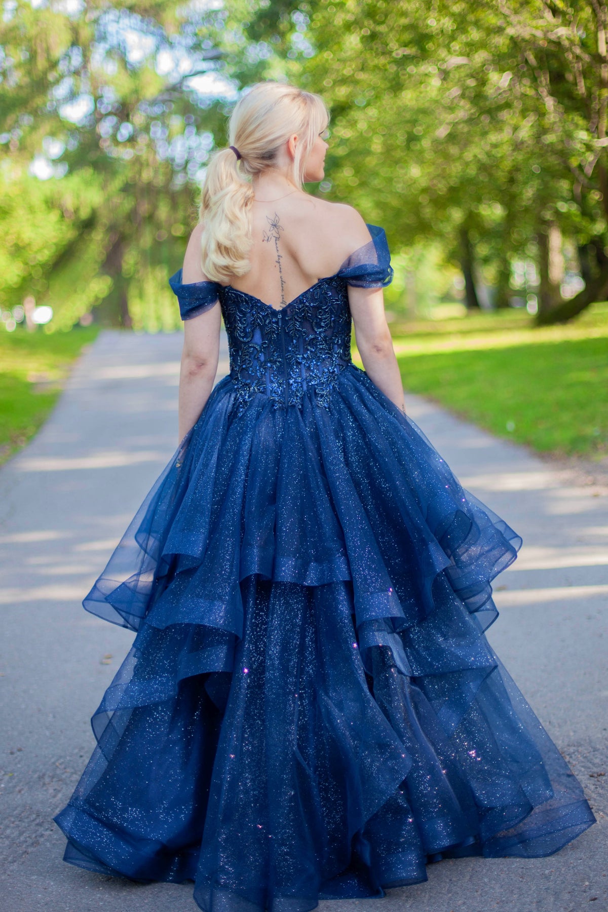 Kimaltava tummansininen vanhojentanssimekko off shoulder -yläosalla ja näyttävällä röyhelöhelmalla.