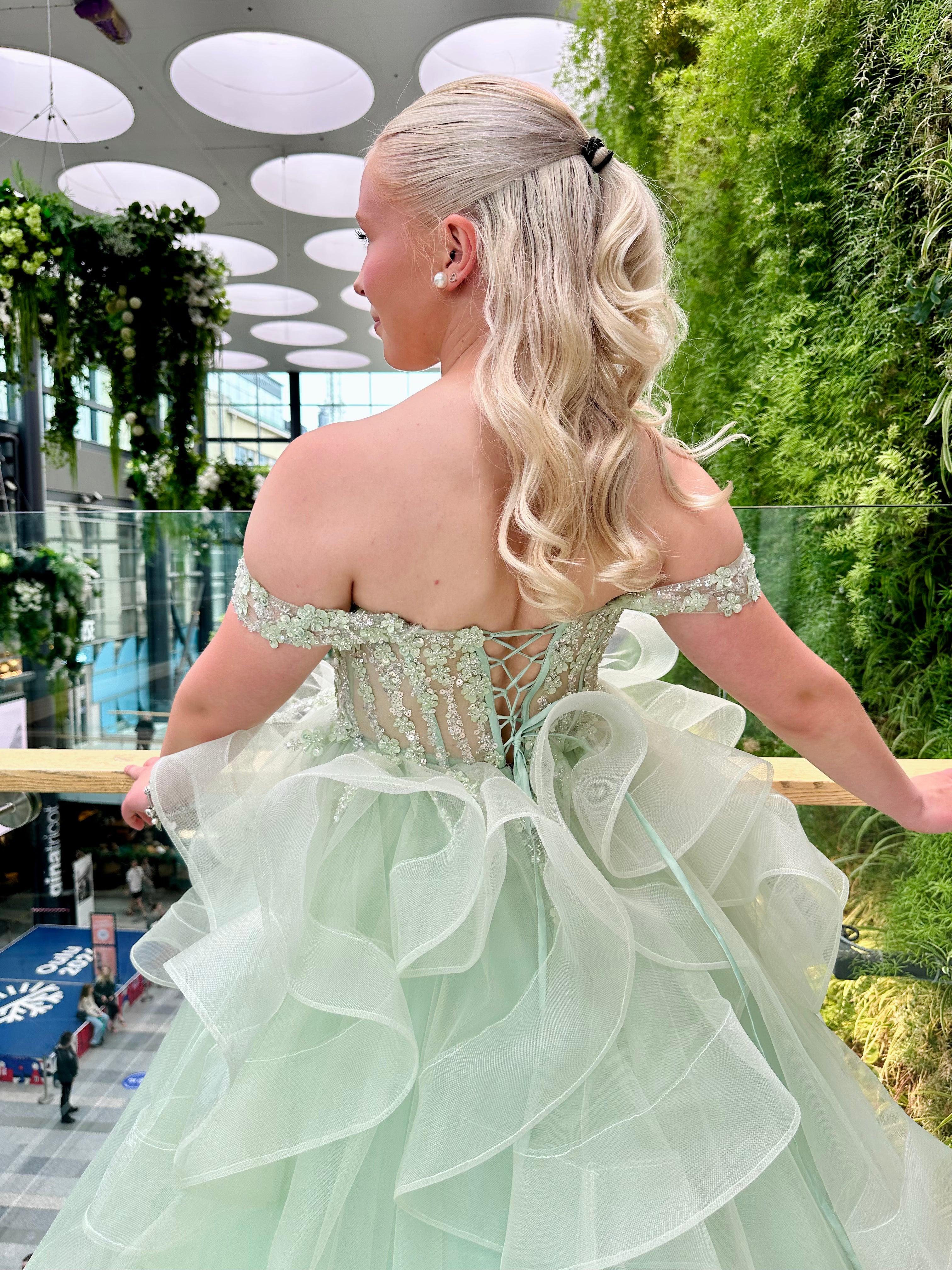 Vaaleanvihreä vanhojentanssimekko röyhelöhelmalla ja off shoulder -mallilla.